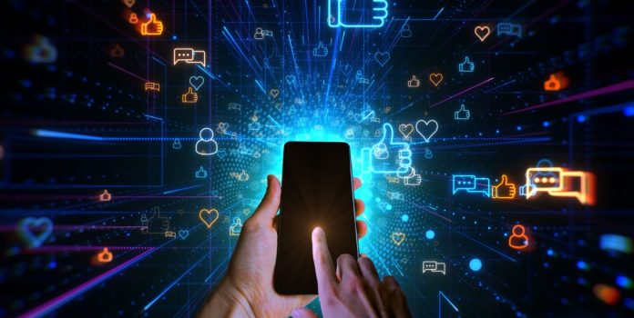 cct-discute-pl-sobre-proibição-da-publicidade-de-apostas Mão segurando celular com fundo escuro cheio de símbolos relacionados a redes sociais