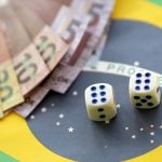 Estudo estima perda de R$ 62,5 bilhões para sites de apostas em 2025 Bandeira do Brasil, dados e dinheiro. A imagem simboliza o ato de apostar entre brasileiros.