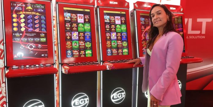Foto de Celina Guedes ao lado de um dos terminais de videoloteria (VLTs) da EGT.