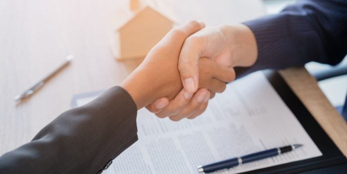 Kaizen-Gaming-anuncia-aquisicao-da-GameplAI Aperto de mãos em frente à mesa com papéis e caneta
