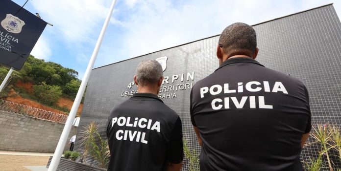 Foto tirada de dois policiais da Polícia Civil, de costas.