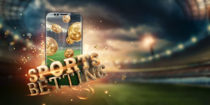 Telefone com moedas virtuais na tela e a escrita Sports Betting na frente frente