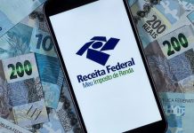 Celular com o logotipo da Receita Federal sobre uma mesa com diversas cédulas de dinheiro