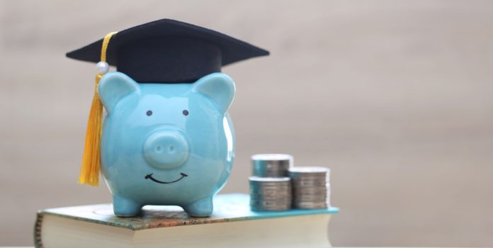 betsul-cartilha-educacao-financeira Cofre de dinheiro azul em formato de porco usando capelo sobre livro e com moedas ao lado