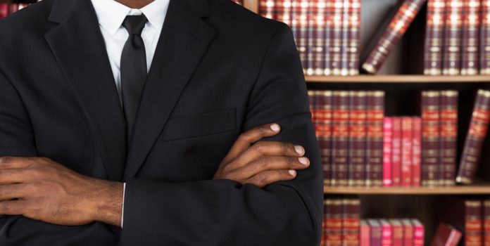 Homem de terno, com os braços cruzados, em frente à estante de livros