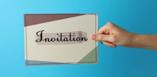 Uma mão segurando um papel escrito 'invitation' em um fundo azul