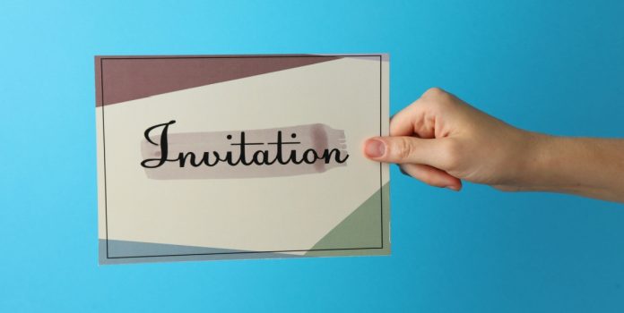 Uma mão segurando um papel escrito 'invitation' em um fundo azul