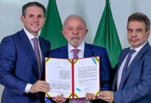 Lei Raul Jungmann determina que bancos e instituições de pagamento bloqueiem contas vinculadas a operadores ilegais Lula segurando o documento oficial da Lei Raul Jungmann ao lado de Hugo Motta e Wellington Lima