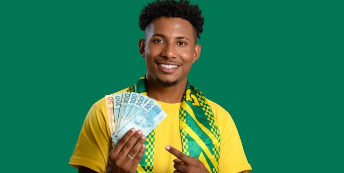aposta-legal-levantamento-ticket-medio-anual-brasil- Homem segurando cédulas de Real com as cores do Brasil em destaque