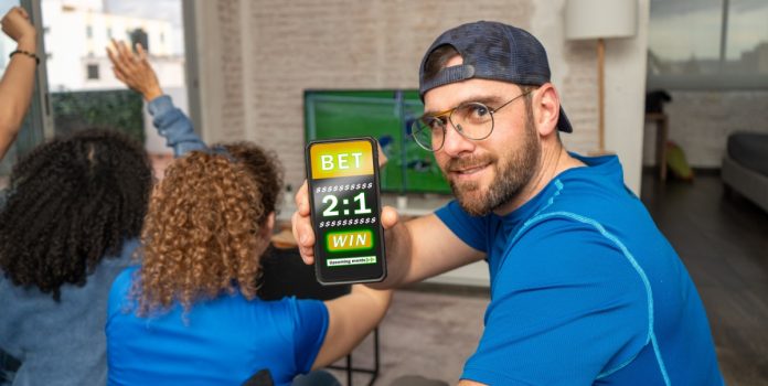 datafolha-levantamento-apostas-brasil Homem mostrando que está apostando no celular vestido de azul ao lado de duas mulheres