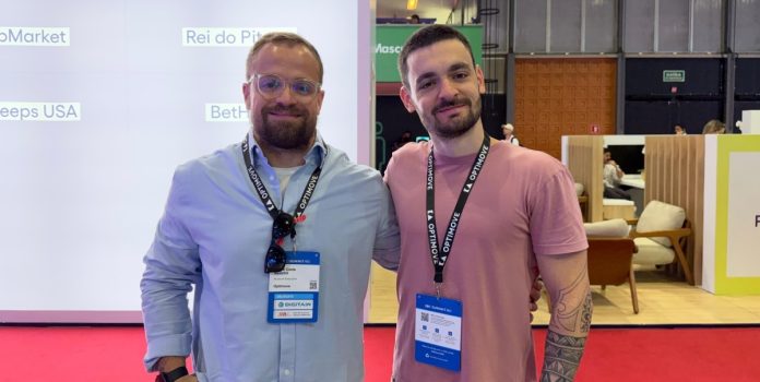 optimove-entrevista-copa-do-mundo-26- Felipe Nadalini e Rafael Alessi, da Optimove, em frente ao estande da empresa no SBC Summit Rio 2026