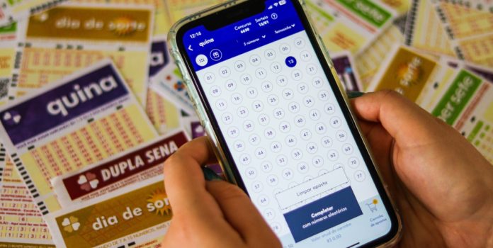 ANEL-propoe-modernizacao-da-Loteria-Federal- Uma pessoa acessando o site da Caixa para apostar na Quina e diveros volantes ao fundo