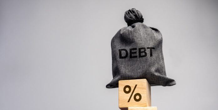 ANJL-destaca-contradicoes-do-Desenrola-2 Um saco com a escrita "debt" em cima de blocos com o símbolo da porcentagem empilhados