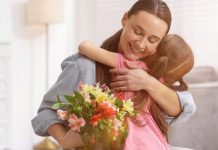 Mãe segurando um buquê de flores e abrançando a filha