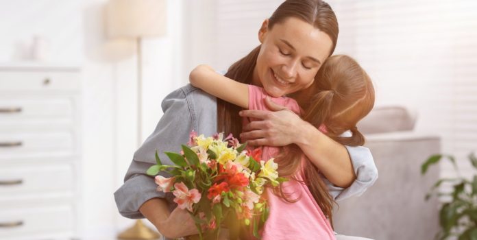 Mãe segurando um buquê de flores e abrançando a filha