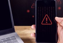 Anatel divulga dados sobre bloqueio de sites de apostas após pedido via LAI Homem segurando um smartphone com símbolo de cuidado em vermelho aparecendo na tela e um notebook desligado ao lado
