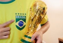 Torcedor vestindo a camiseta do Brasil com cinco estrelas e segurando réplica do troféu da Copa do Mundo FIFA.