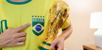Torcedor vestindo a camiseta do Brasil com cinco estrelas e segurando réplica do troféu da Copa do Mundo FIFA.
