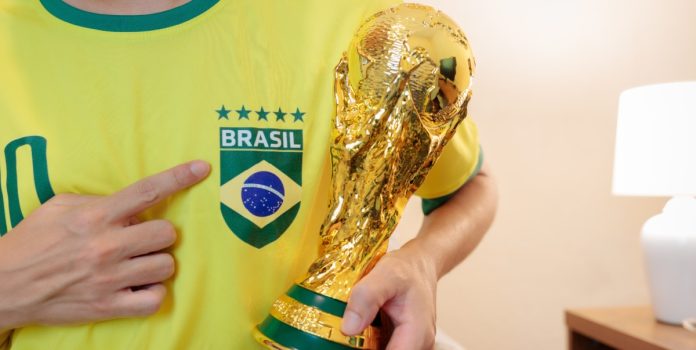HSR-lanca-5a-edicao-do-RMG-Brand-Tracking-sobre-apostas-no-Brasil Torcedor vestindo a camiseta do Brasil com cinco estrelas e segurando réplica do troféu da Copa do Mundo FIFA.