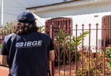 Pesquisador do IBGE espera em frente de residência.