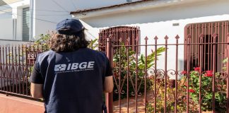 Pesquisador do IBGE espera em frente de residência.