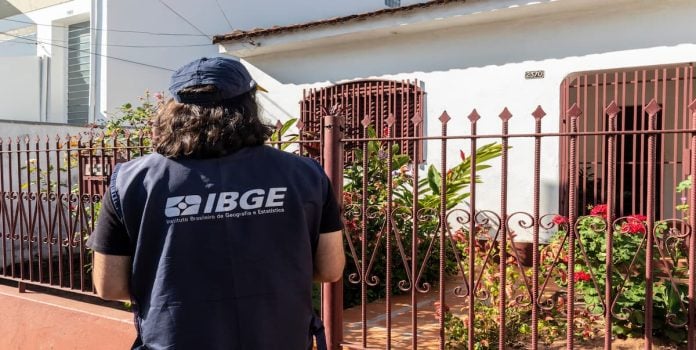 IBGE Pesquisador do IBGE espera em frente de residência.