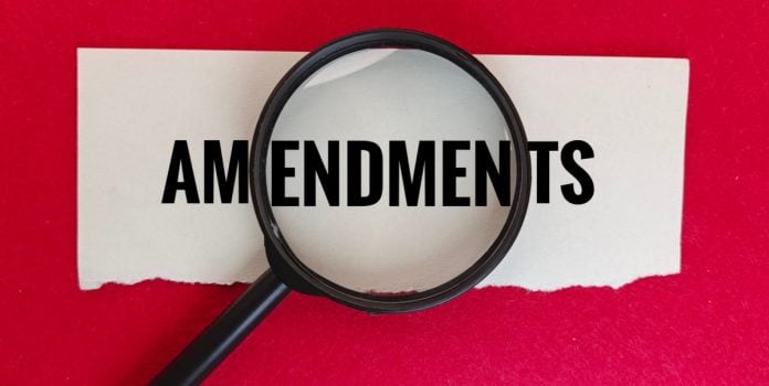 Papel rasgado com a escrita "Amendments" sobre a mesa vermelha e com uma lupa no centro