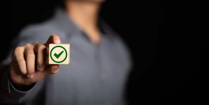 Pesquisa-da-Genial-Investimentos-aponta-apoio-a-restricao-de-apostas-no-Desenrola-2.0 Um homem segurando um bloco de madeira com o símbolo verde de aprovado em direção à câmera