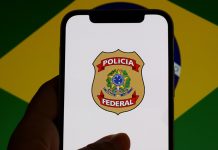 SPA determina repasse de recursos de apostas ao Funapol via DARF 5862 Um celular mostrando o brasão da Polícia Federal com a bandeira do Brasil desfocada ao fundo