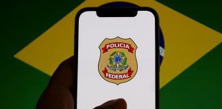 SPA determina repasse de recursos de apostas ao Funapol via DARF 5862 Um celular mostrando o brasão da Polícia Federal com a bandeira do Brasil desfocada ao fundo