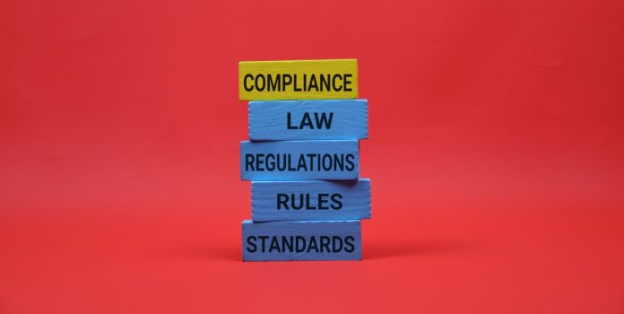 Blocos empilhados sobre conformidade regulatória, lei, regulação, regras e padrões com fundo vermelho