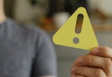 Homem segurando um sinal de alerta amarelo em direção à câmera