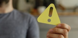 TCU aponta fragilidades no combate à lavagem de dinheiro no mercado de apostas Homem segurando um sinal de alerta amarelo em direção à câmera