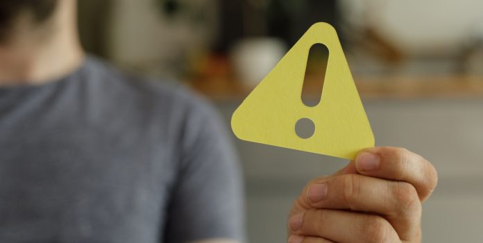 Homem segurando um sinal de alerta amarelo em direção à câmera