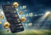 Um celular projetado em frente a um campo de futebol apresentando opções de apostas esportivas na tela