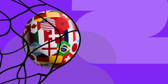 Uma bola de futebol, estampada com bandeiras de diferentes países, batendo na rede do gol sobre um fundo roxo