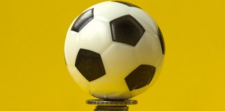 Uma bola de futebol em cima de uma pilha de moedas e com fundo amarelo