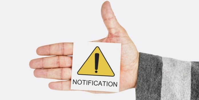 AGU-solicita-remocao-imediata-de-perfis-no-YouTube-que-promovem-apostas-ilegais Uma mão segurando um papel escrito notificação em inglês com um símbolo amarelo de alerta