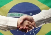 Aperto de mãos em frente à bandeira do Brasil