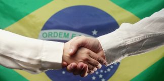 Atlaslive anuncia parceria com a FIRST.bet para fortalecer solução de apostas esportivas Aperto de mãos em frente à bandeira do Brasil