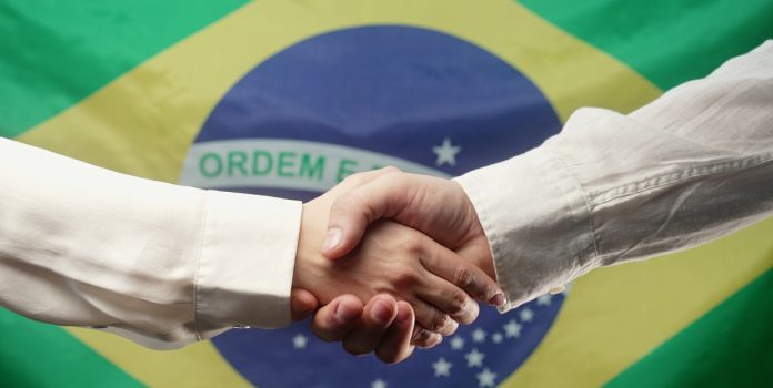 Aperto de mãos em frente à bandeira do Brasil