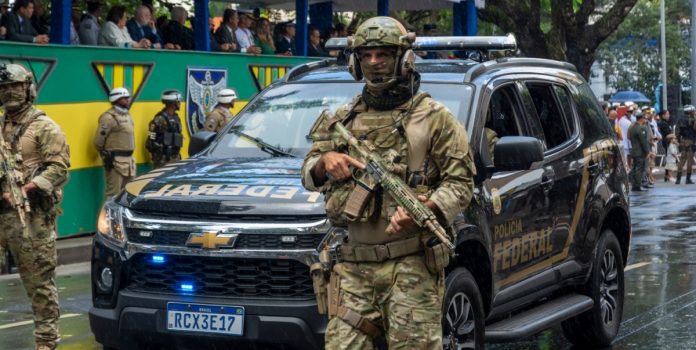 Policial Federal armado na rua em frente ao carro da Polícia Federal