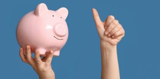 Executivos e especialistas apontam benefícios do setor de apostas para sociedade Uma pessoa segurando um cofrinho de porco com uma mão e fazendo o sinal de joinha com a outra em um fundo azul
