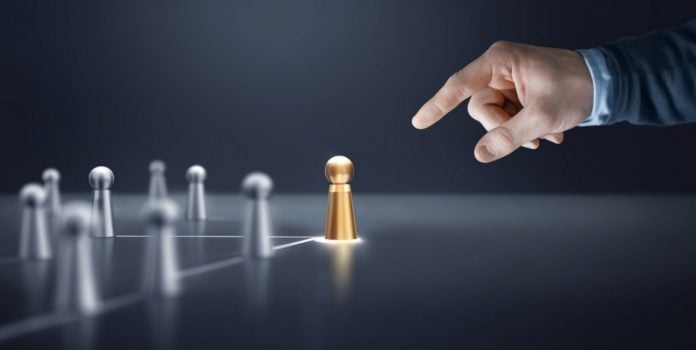 Flutter-Brazil-fortalece-quadro-de-lideres-com-duas-nomeacoes Uma mão apontando para bonecos de prata e de ouro sobre uma mesa, representando um líder e sua equipe