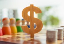 Incoerência entre discurso e prática: quais são as prioridades do governo para o mercado de apostas? O símbolo de madeira do dólar entre bonecos de madeira e pilhas de moedas sobre o tabuleiro de xadrez