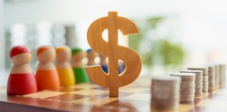 O símbolo de madeira do dólar entre bonecos de madeira e pilhas de moedas sobre o tabuleiro de xadrez