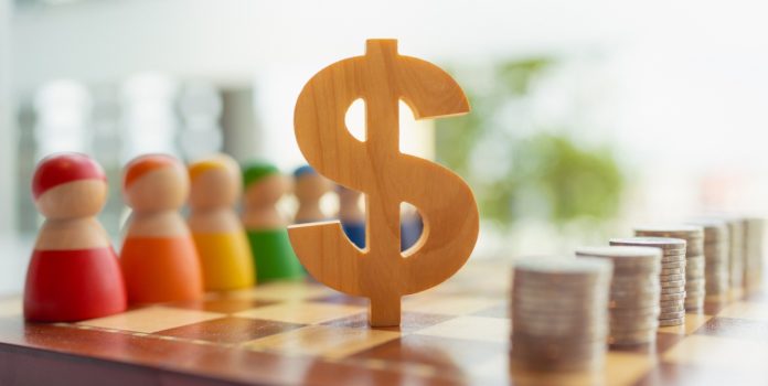 O símbolo de madeira do dólar entre bonecos de madeira e pilhas de moedas sobre o tabuleiro de xadrez