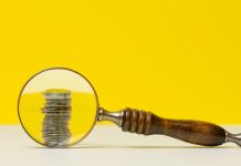 MPF defende aumento do percentual das apostas destinado ao SUS Uma lupa destacando uma pilha de moedas em um fundo amarelo