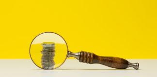 MPF defende aumento do percentual das apostas destinado ao SUS Uma lupa destacando uma pilha de moedas em um fundo amarelo