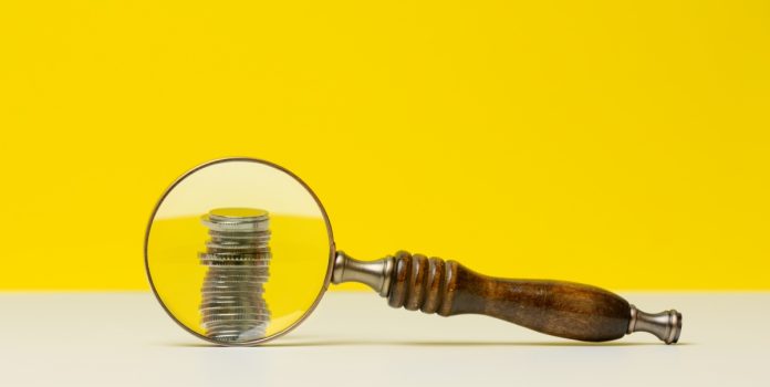 Uma lupa destacando uma pilha de moedas em um fundo amarelo